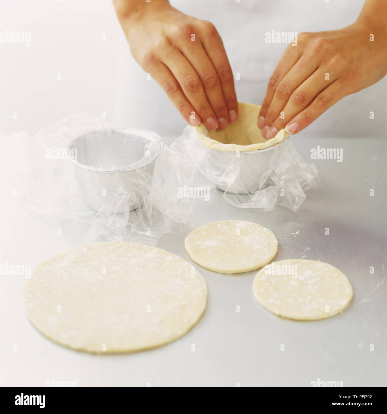 Lining dariole moulds with layers of cling film and pastry dough Stock
