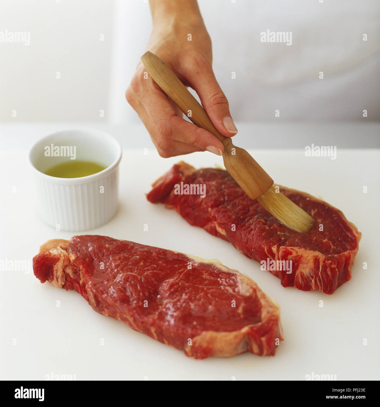 Brushing two raw steaks with oil Stock Photo Alamy