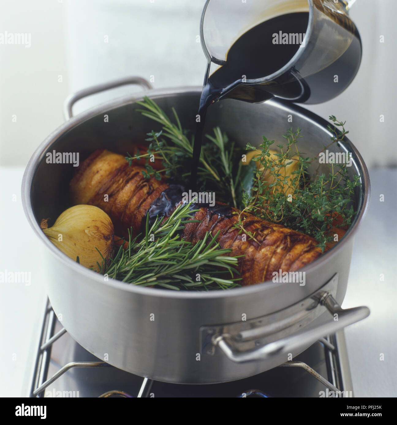Pouring sauce over braised pork belly, onions and fresh herbs in a pan