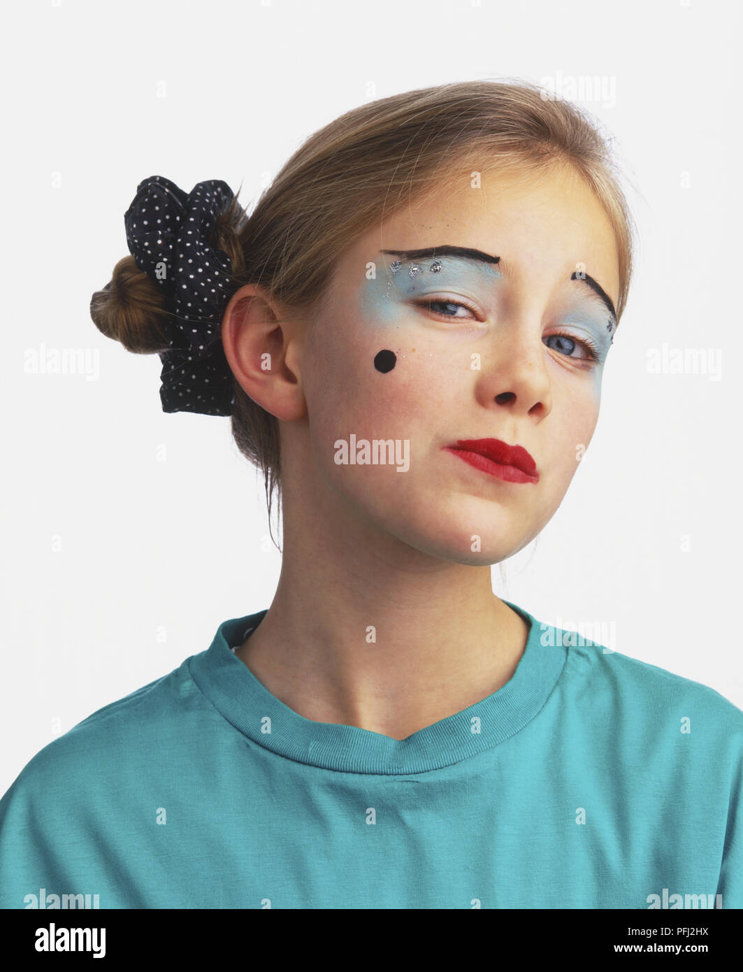 Headshot of girl wearing eye make up, red lipstick and beauty spot, hair tied in scrunchy, head cocked, looking at camera Stock Photo
