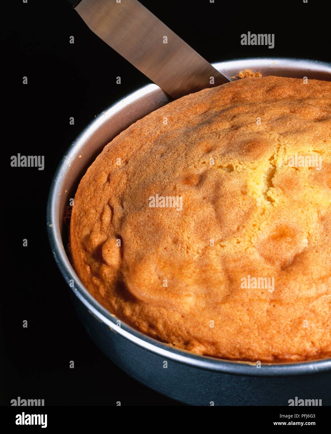 Edges of a sponge cake being loosened from the tin with a palette knife, close-up Stock Photo