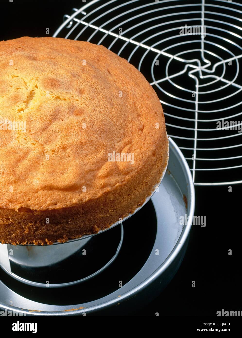 Baked sponge cake being removed from tin, cooling rack nearby, close-up Stock Photo