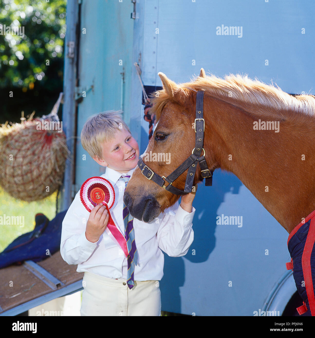 Great Britain, England, a blonde boy holding a red rosette and stroking his pony Stock Photo