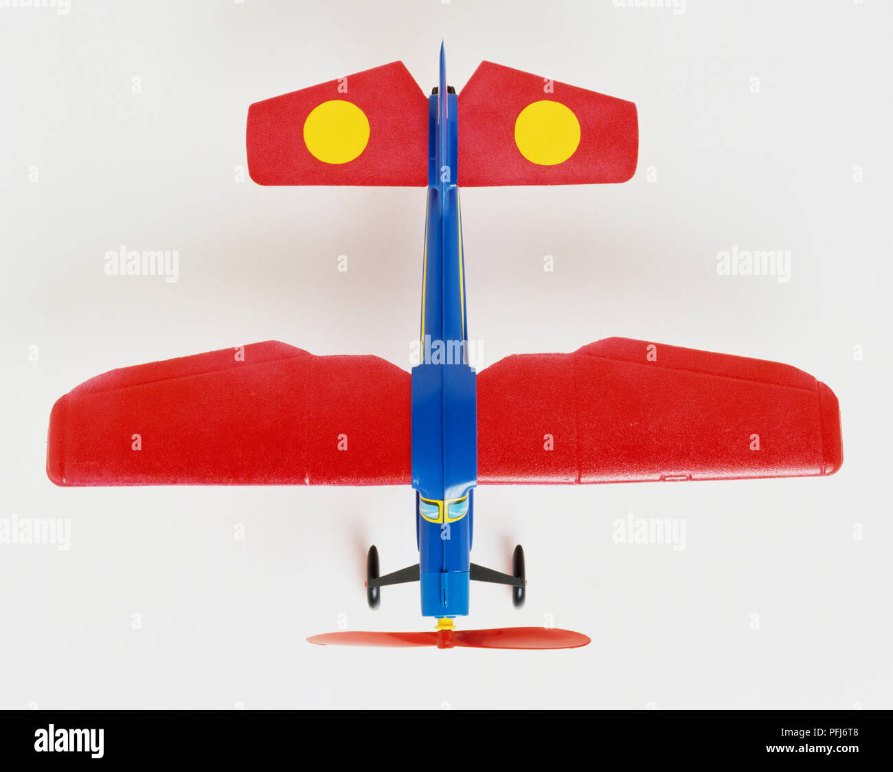 Colourful toy propeller plane, red wings blue body, yellow dots on tail wings, overhead view. Stock Photo