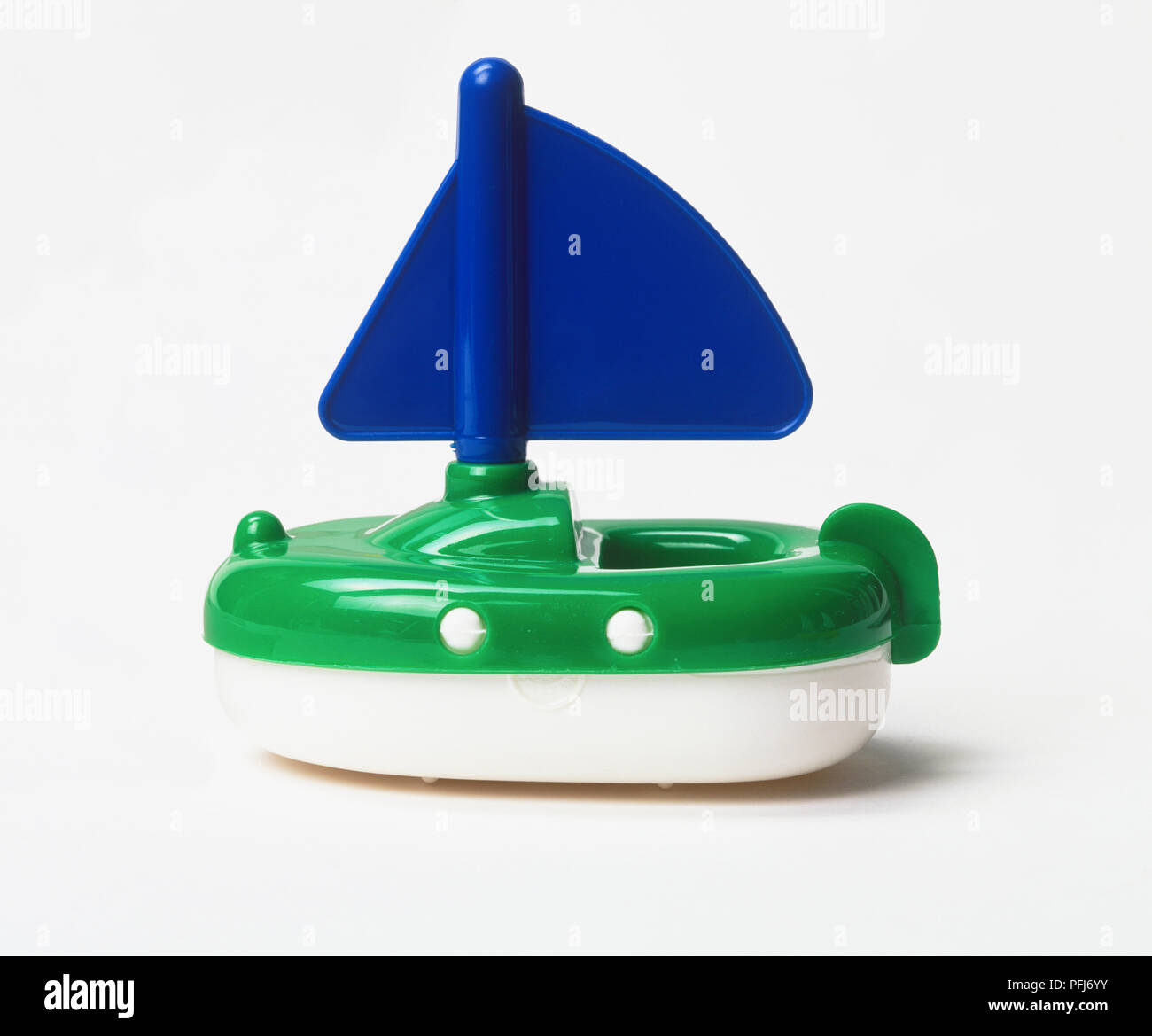 Green and white plastic boat with blue sail Stock Photo