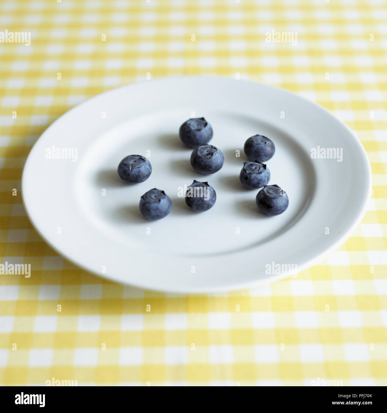 Vaccinium sp., Blue Berries, plate of blue berries on yellow chequered cloth. Stock Photo