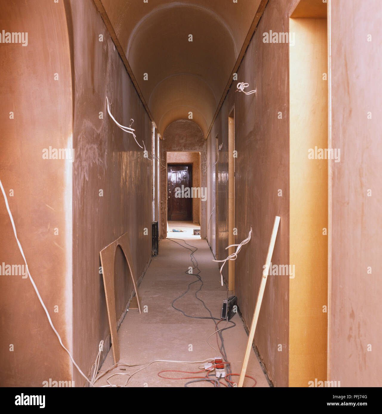 Corridor of building undergoing refurbishment, stripped walls, wires and leads stretched across floor, wooden fittings resting on wall. Stock Photo