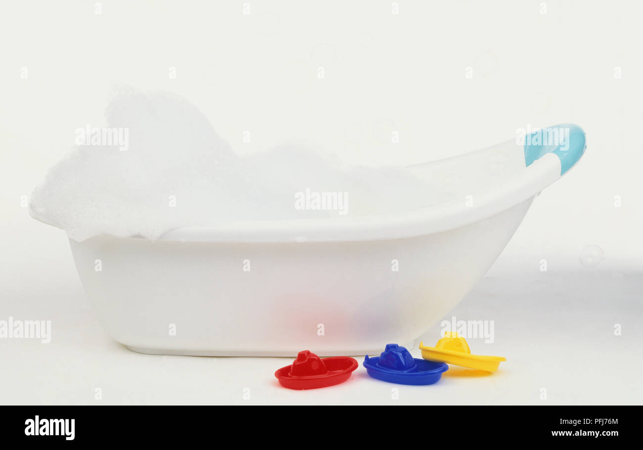 Baby's bath filled with soap suds, three plastic boats on floor in front, side view Stock Photo