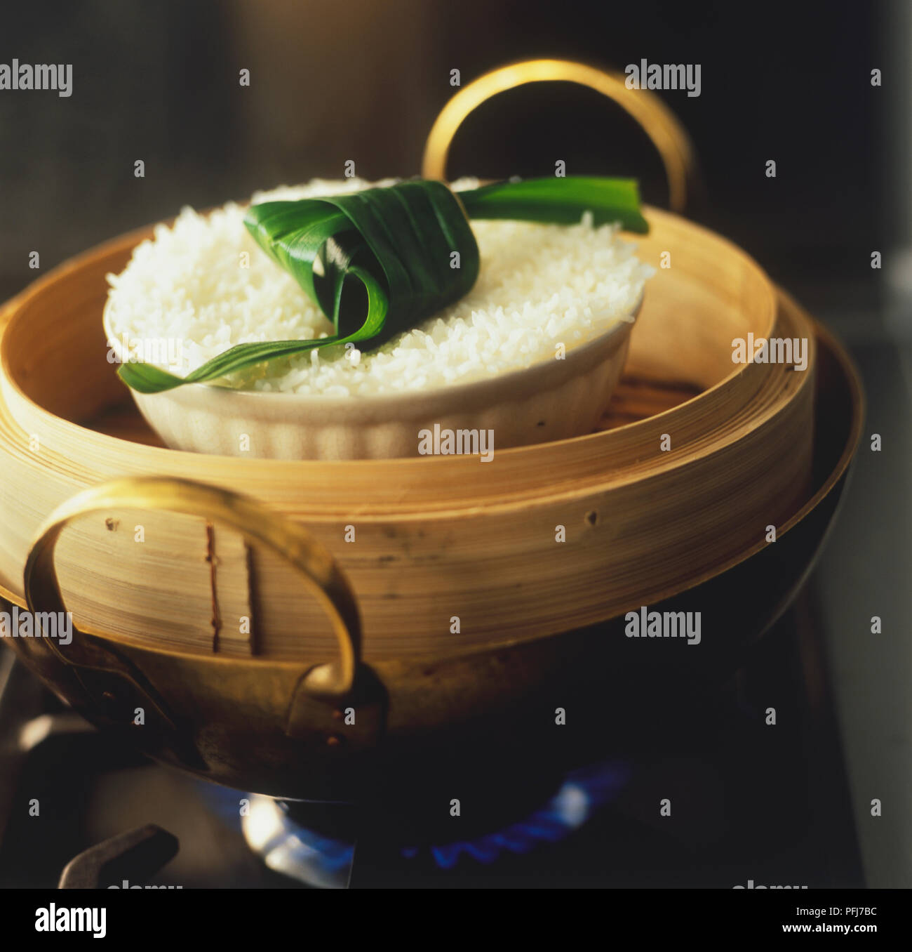 Kao suay, bowl of steam-cooked white jasmine rice, garnished with a folded pandanus leaf, on a gas stove Stock Photo