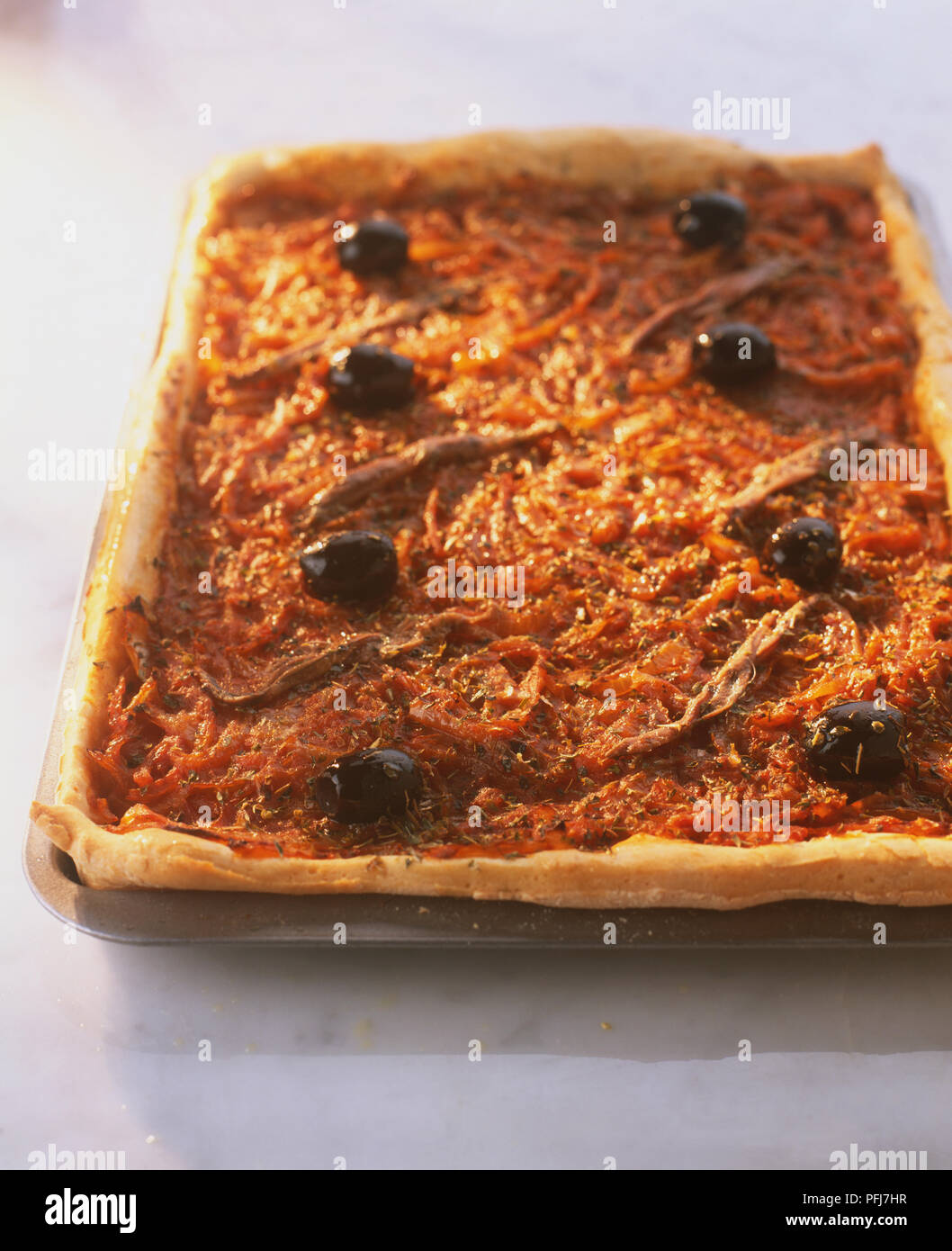 Pissaladiere Pizza, on rectangular baking tray, with crispy, risen crust, topped with onions, anchovies and olives Stock Photo