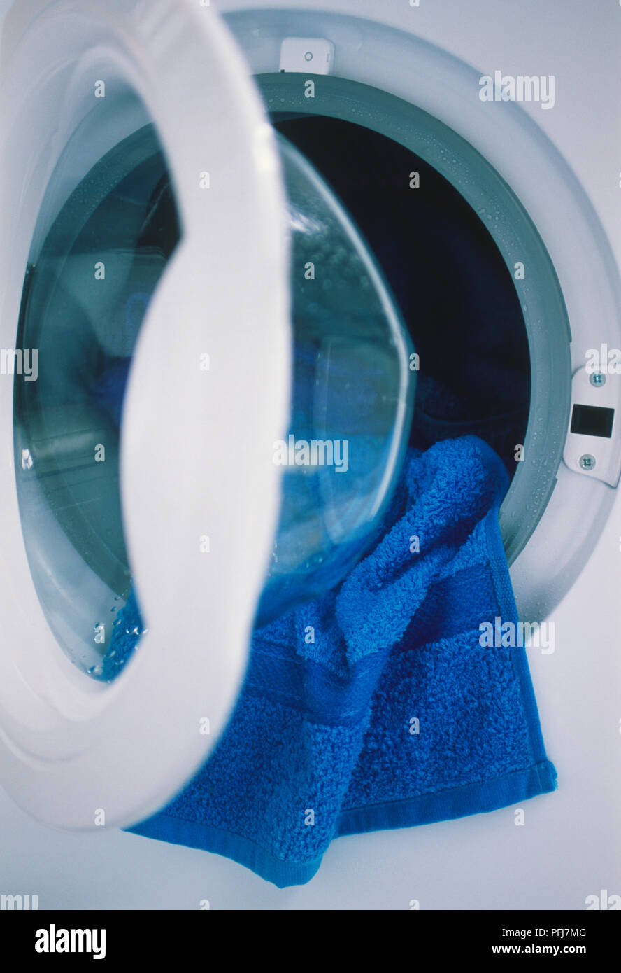 Blue towel hanging out of half open washing machine door Stock Photo