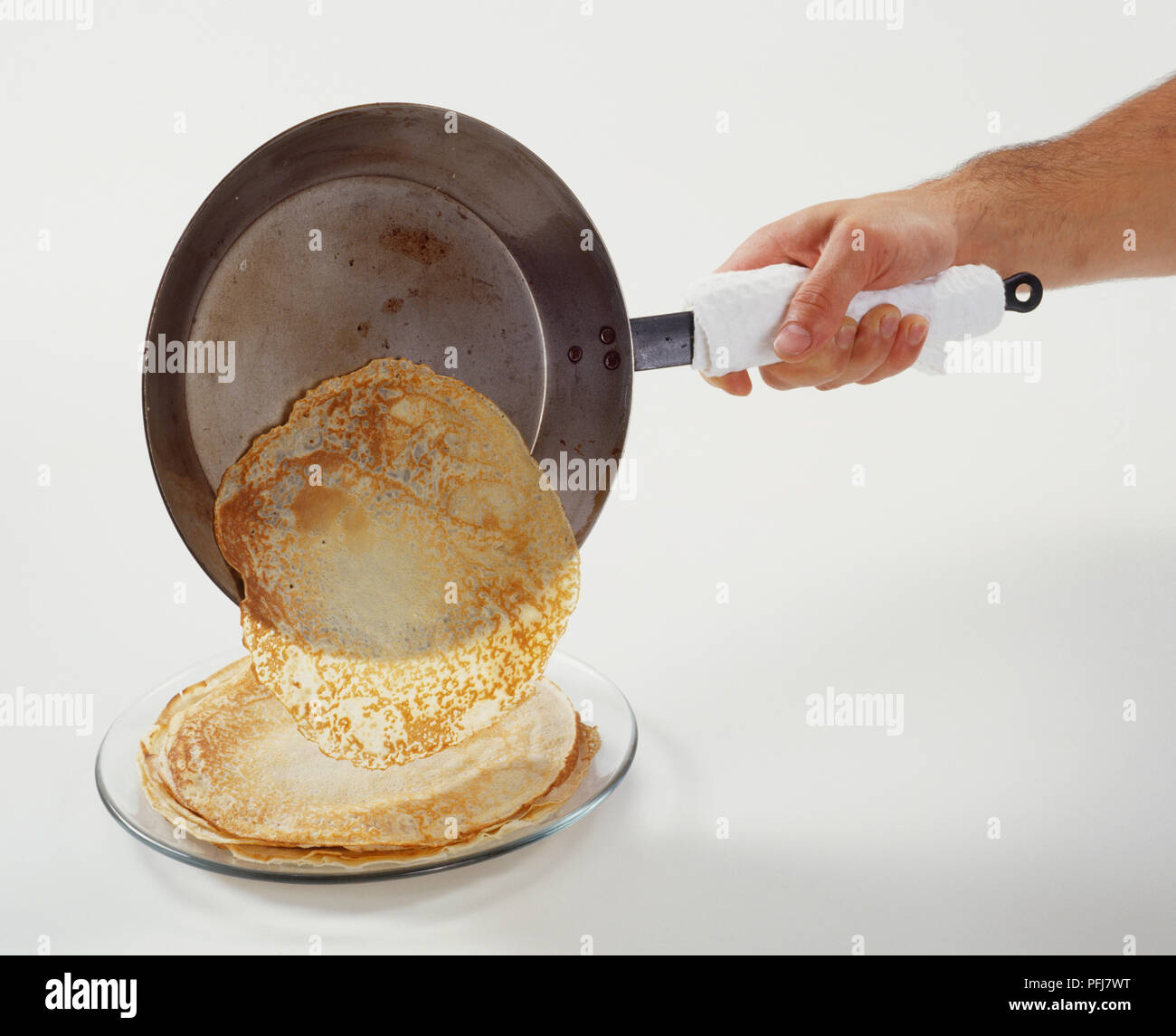 Person holding handle of pan from which crepe is sliding onto pile on plate Stock Photo