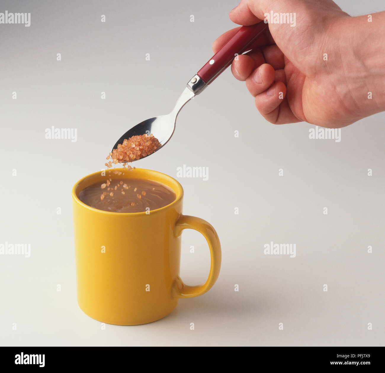 Brown sugar being spooned into mug of coffee Stock Photo