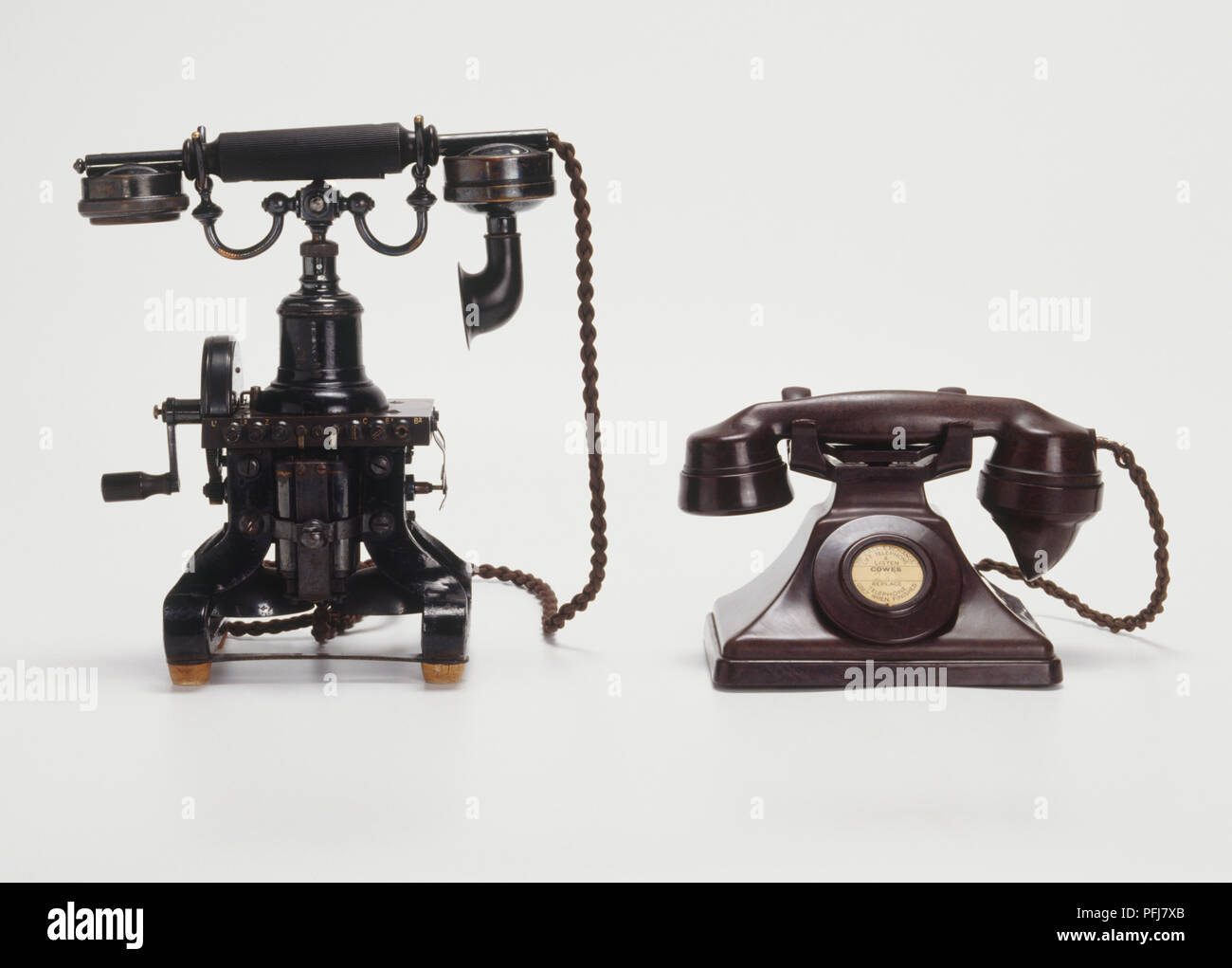 Two old, black desk phones, large mouthpieces, receiver across top, one with side crank Stock Photo