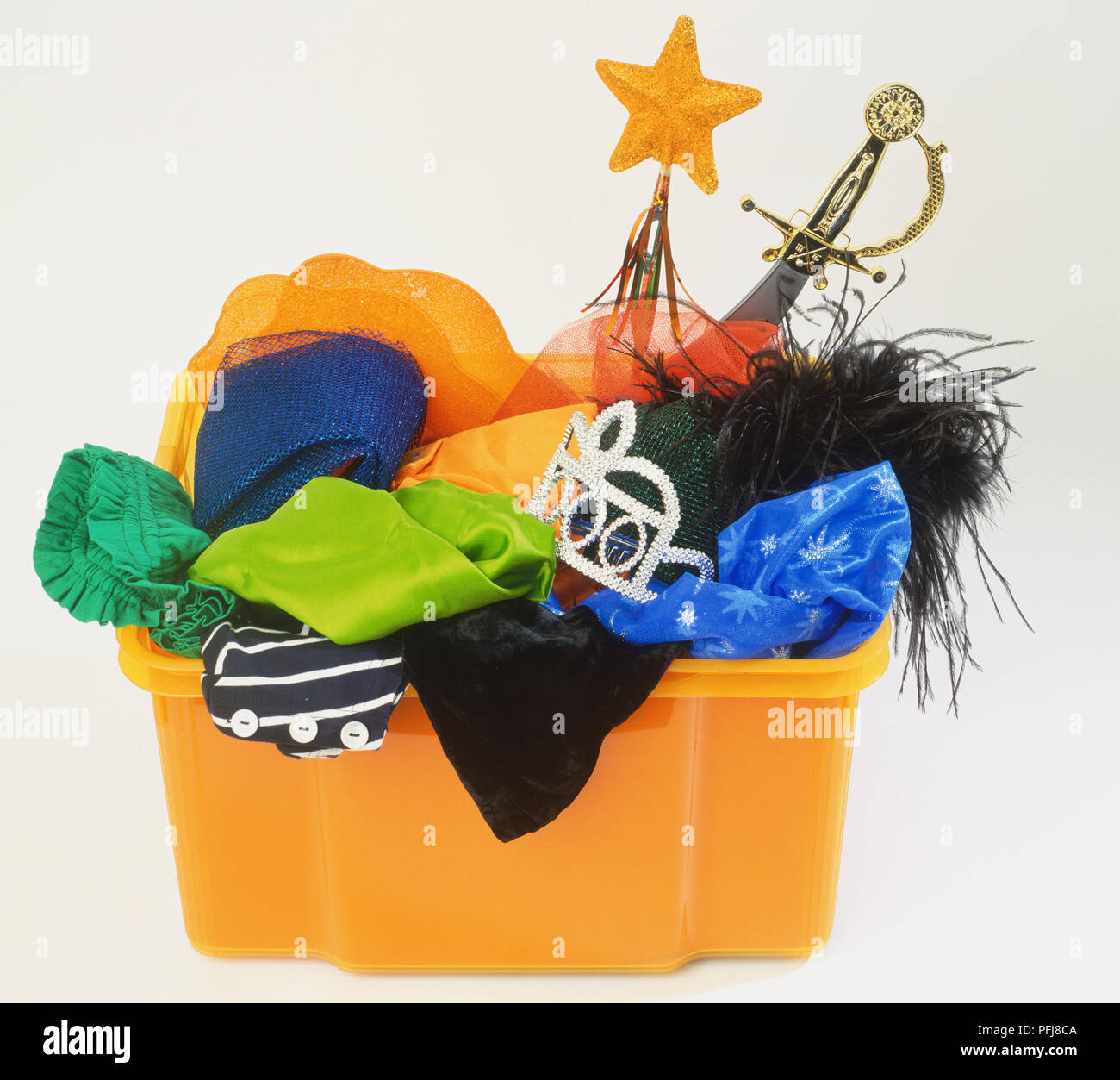 Orange plastic container filled with selection of fancy dress accessories and props, front view. Stock Photo