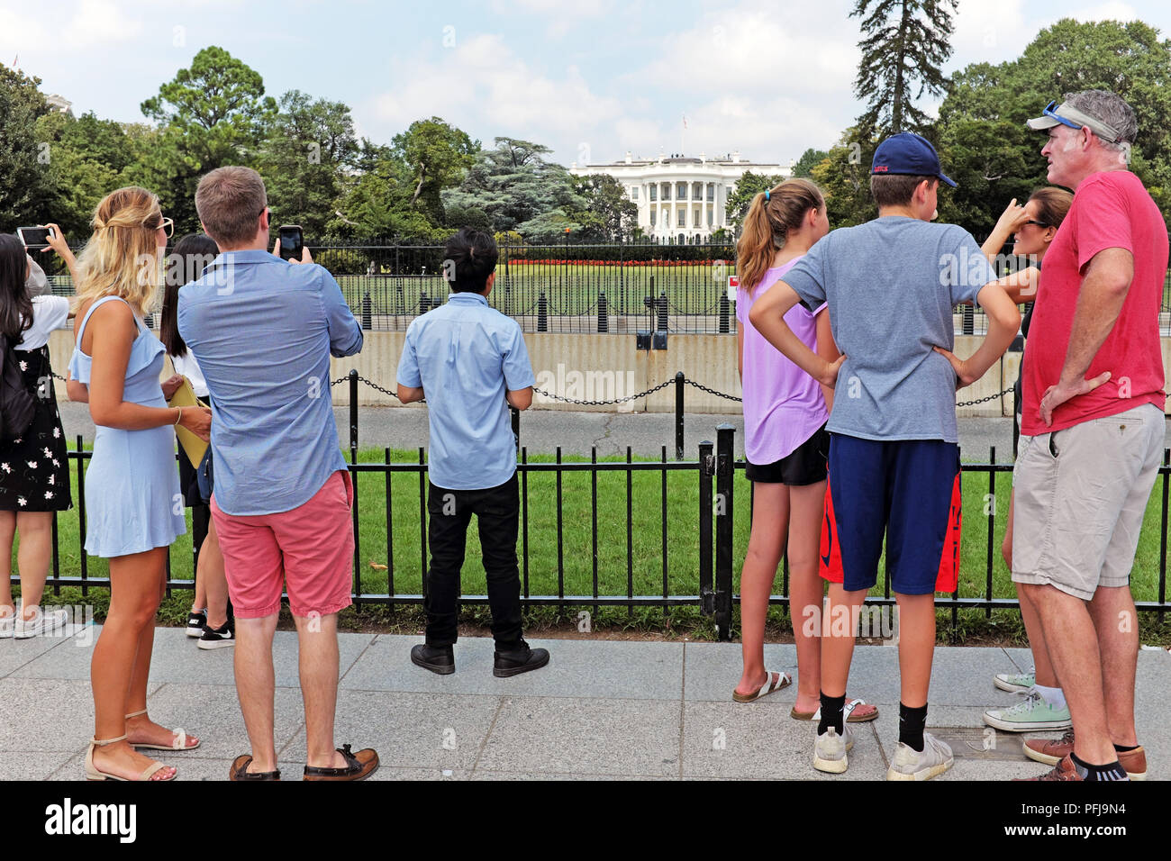 Summer tourists stand and take photos of the distant U.S. White House from behind the security barriers in Washington D.C. USA. Stock Photo
