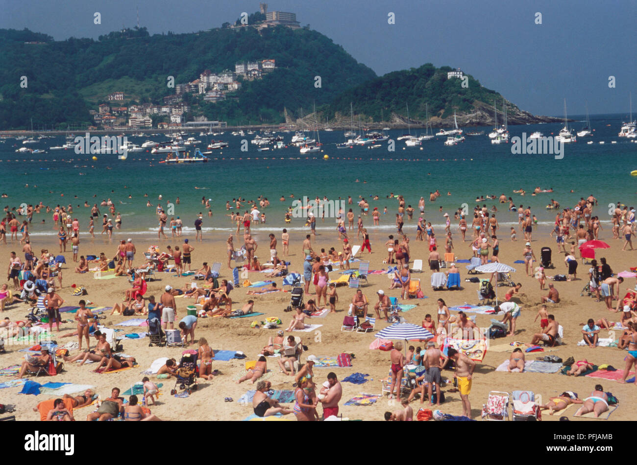 Europe, Spain, Northern Spain, San Sebastian, La Concha, sandy bay full of sunbathers, swimmers and boats in sea Stock Photo