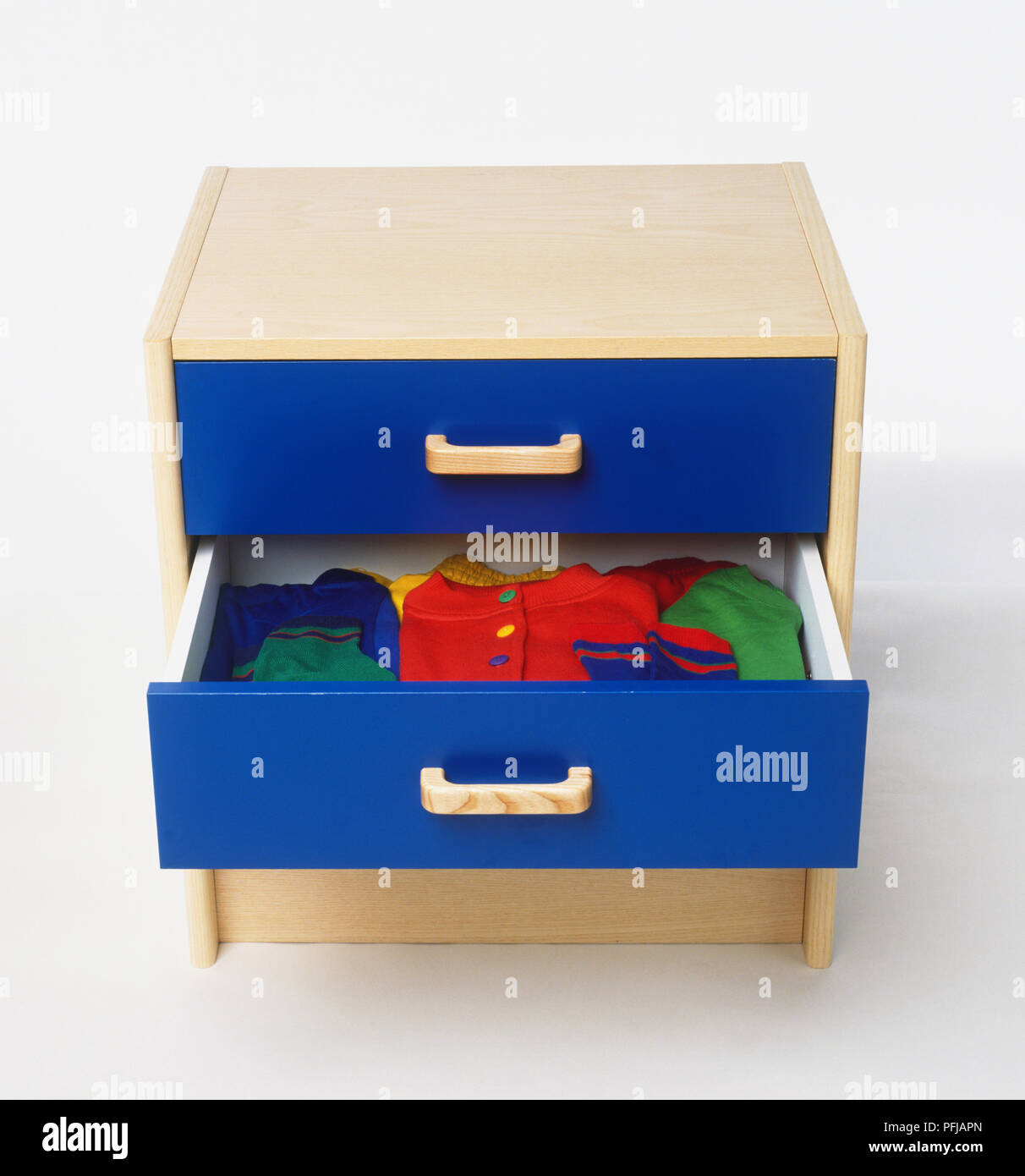 Small chest of drawers with one drawer pulled out, showing folded childrens' clothes, high angle view Stock Photo