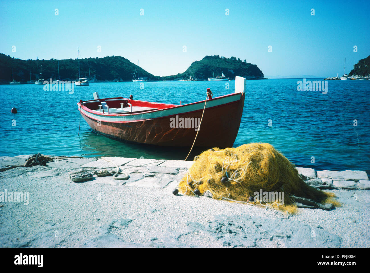 Greek fishing boat moored in a bay, fishing nets on shore Stock Photo