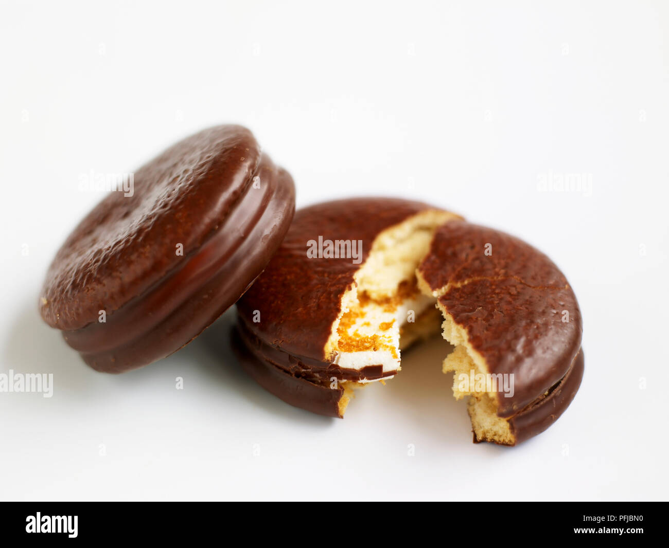 Two chocolatecovered marshmallow teacakes, one broken in half Stock
