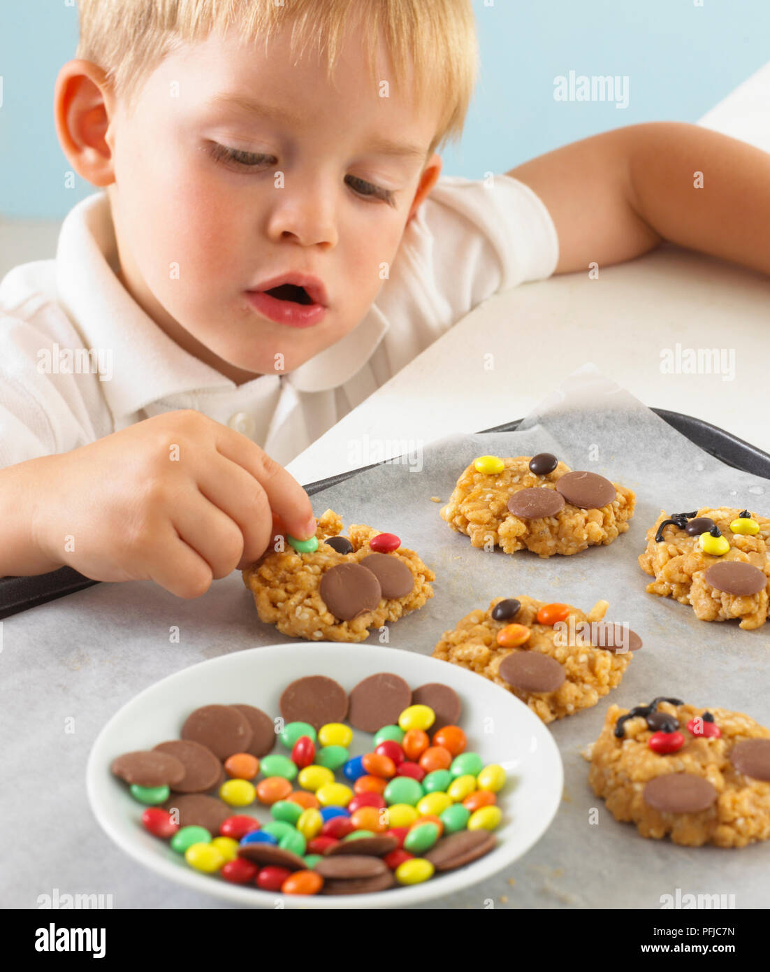 Boy decorating puffed rice and peanut cookies with coloured chocolates Stock Photo