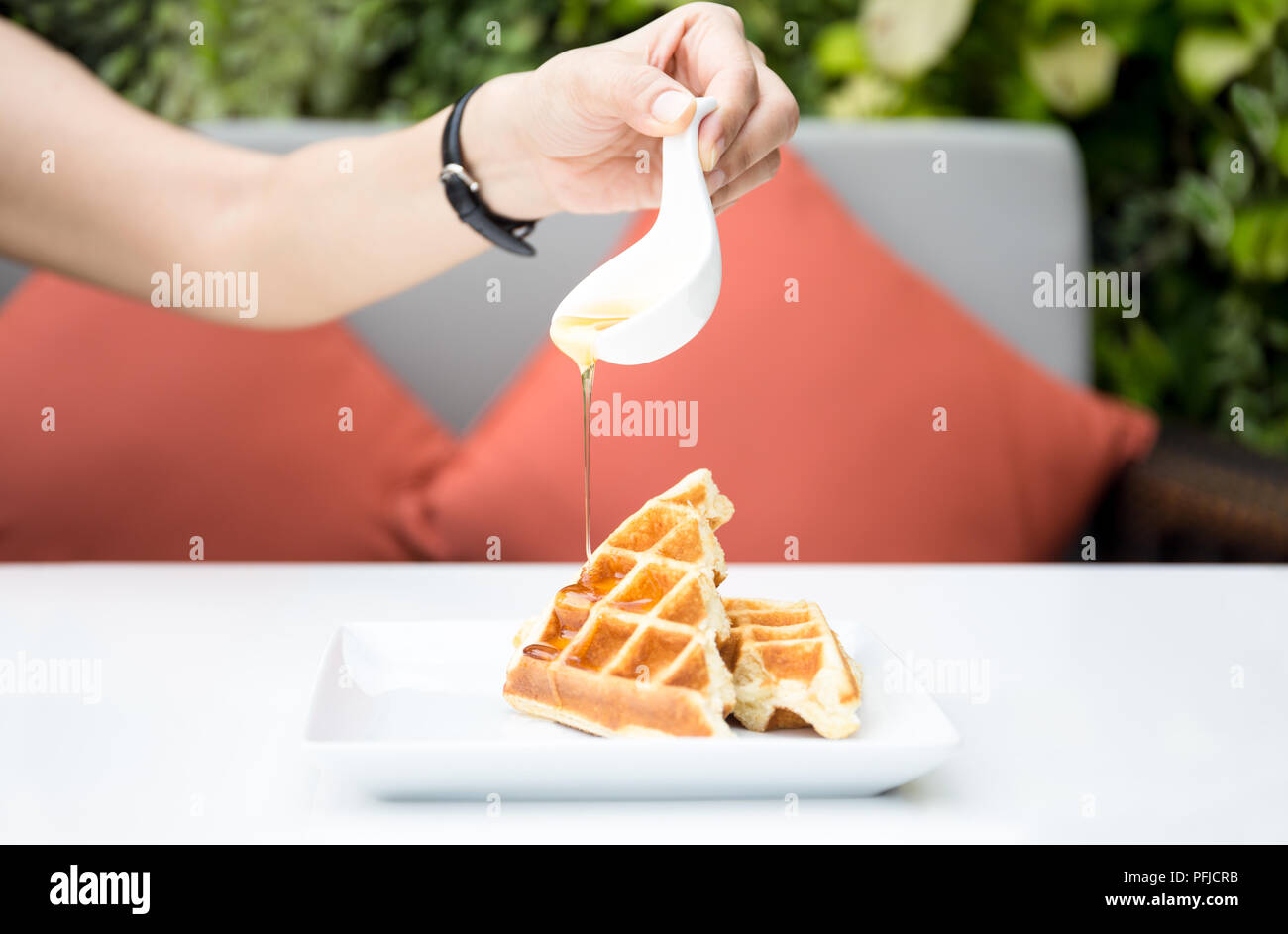 Woman hand pouring honey on fresh waffles at breakfast time Stock Photo