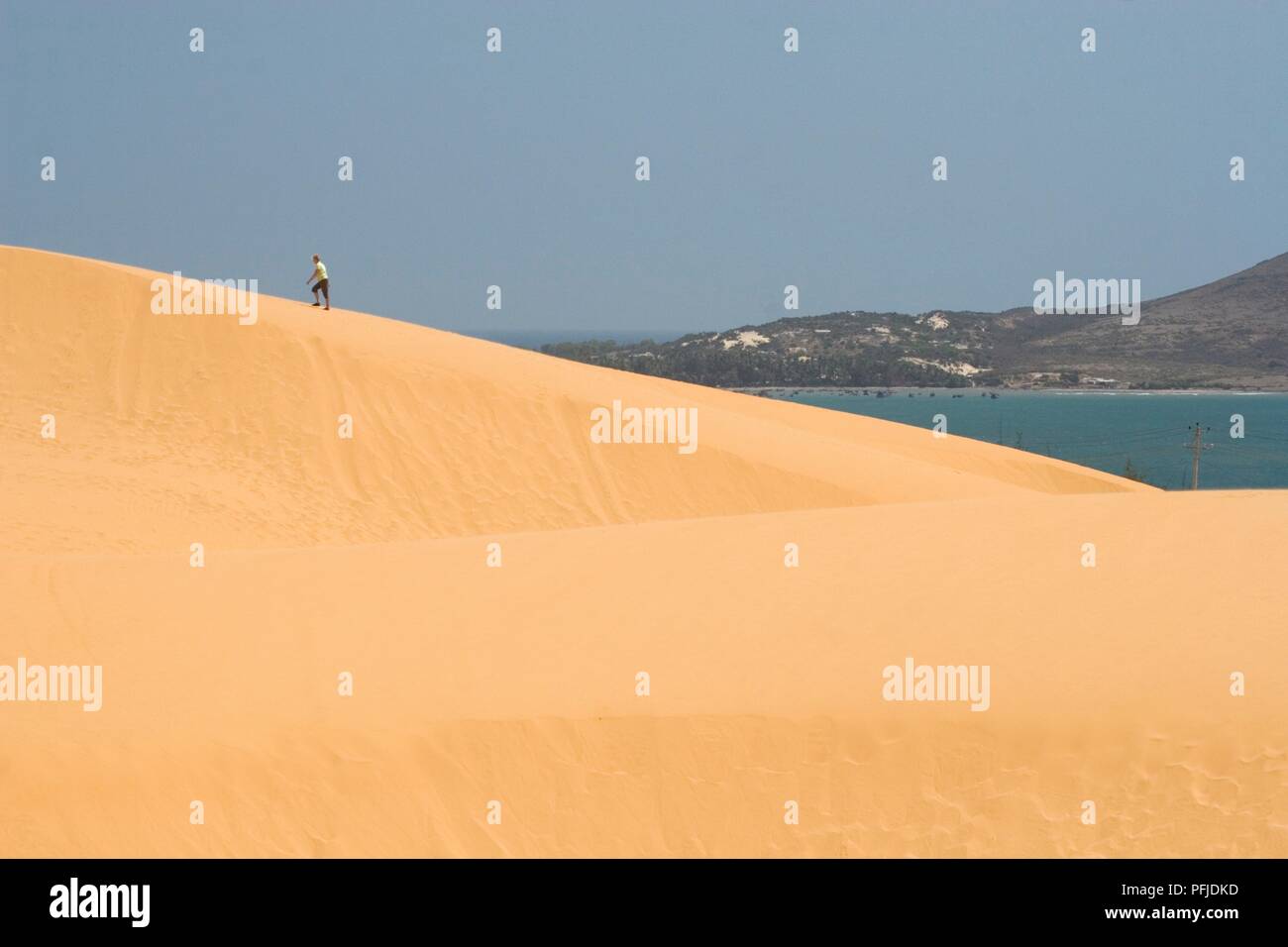Vietnam, Phan Thiet, Mui Ne Beach, Bao Trang, man climbing golden sand dunes by a lake Stock Photo