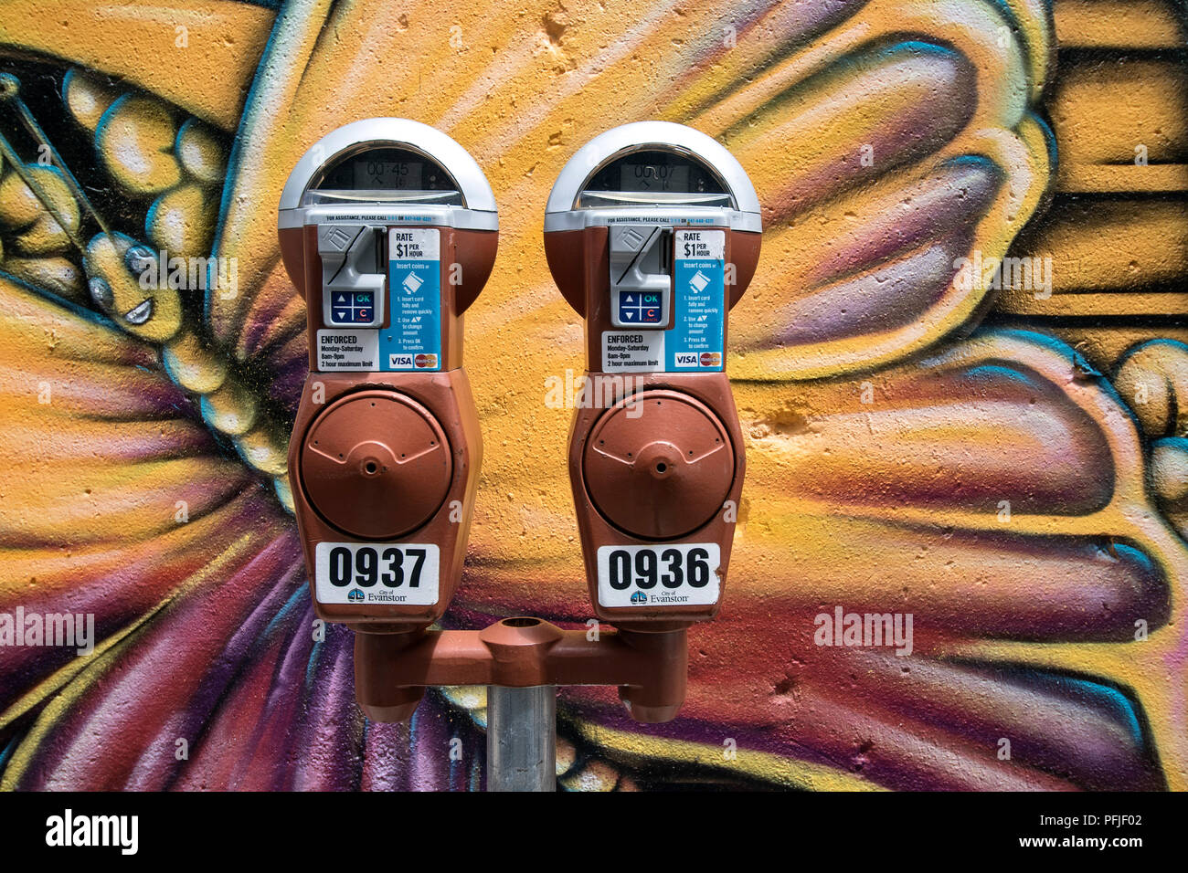 Parking meter in front of a wall with butterfly graffiti in Evanston, Illinois, USA. Stock Photo