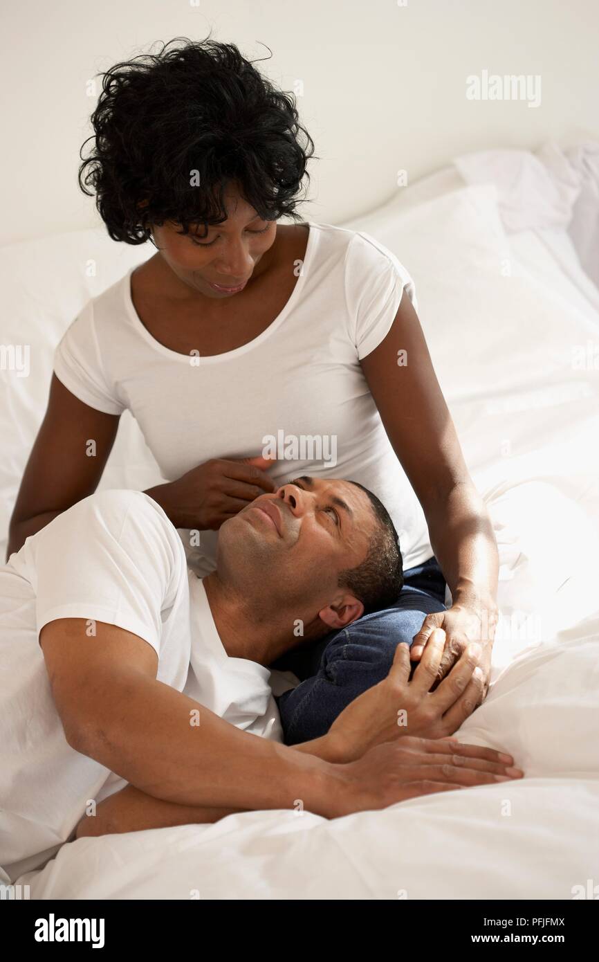 Head of man resting on lap of woman sitting on bed Stock Photo