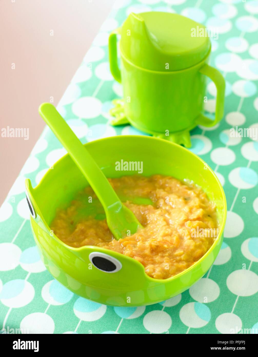 Lentil and carrot puree in green bowl with spoon embedded, and green mug with spout Stock Photo