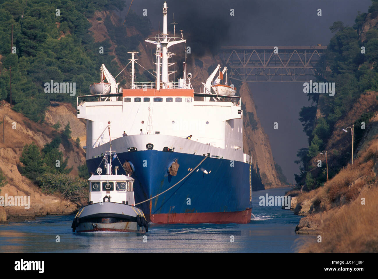 Greece, Peloponnese, tugboat guiding ship through the Corinth Canal, with railroad bridge overhead Stock Photo