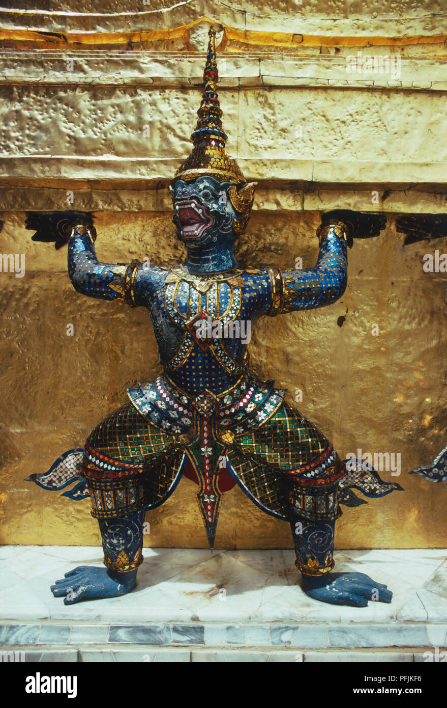 Thailand, Bangkok, statue with legs wide and arms lifted in front of a gilded wall Stock Photo