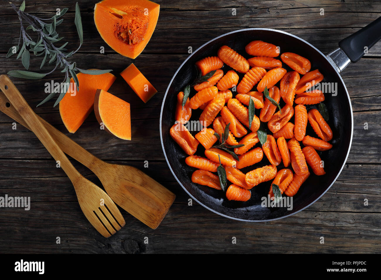 pumpkin gnocchi fried in butter with fresh sage leaves in skillet. pieces of pumpkin and wooden spatulas on old dark wooden table, horizontal view fro Stock Photo