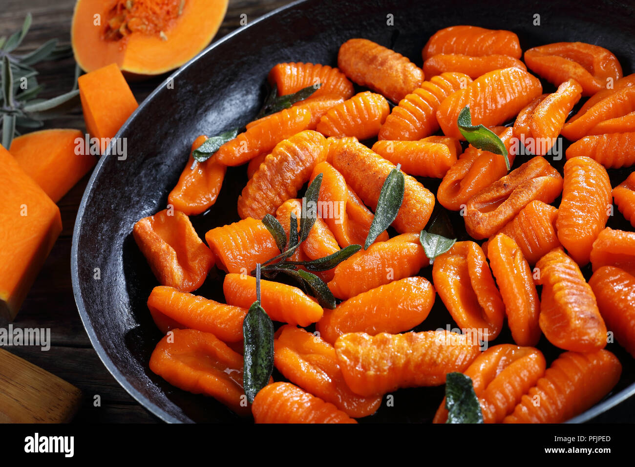tasty pumpkin gnocchi fried in butter with fresh sage leaves in a frying pan. pieces of pumpkin on old dark wooden boards, horizontal view from above, Stock Photo