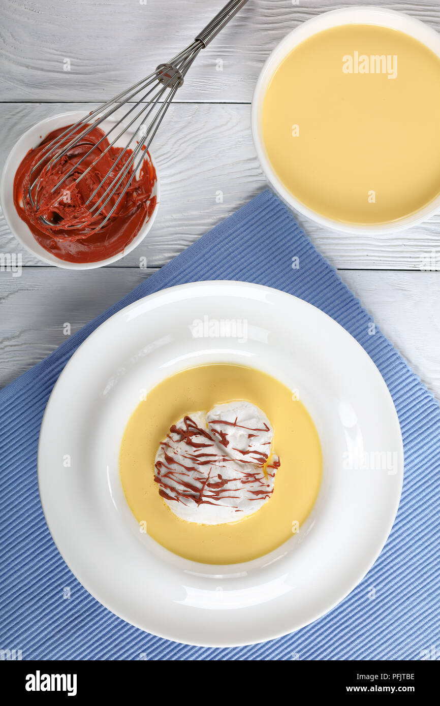 a floating island or birds milk, consisting of meringue floating on creme anglaise and drizzled with chocolate ganache, classic recipe, ingredients at Stock Photo