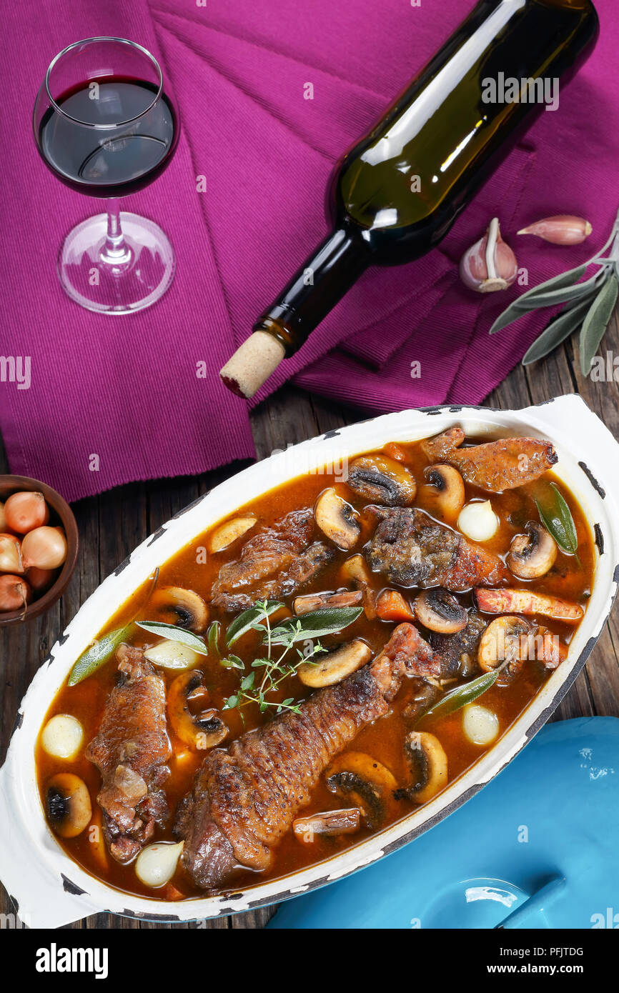 festive dinner recipe - a rooster stewed in red wine with spice, herbs, authentic french recipe - coq au vin. a bottle of wine, corkscrew, a glass wit Stock Photo