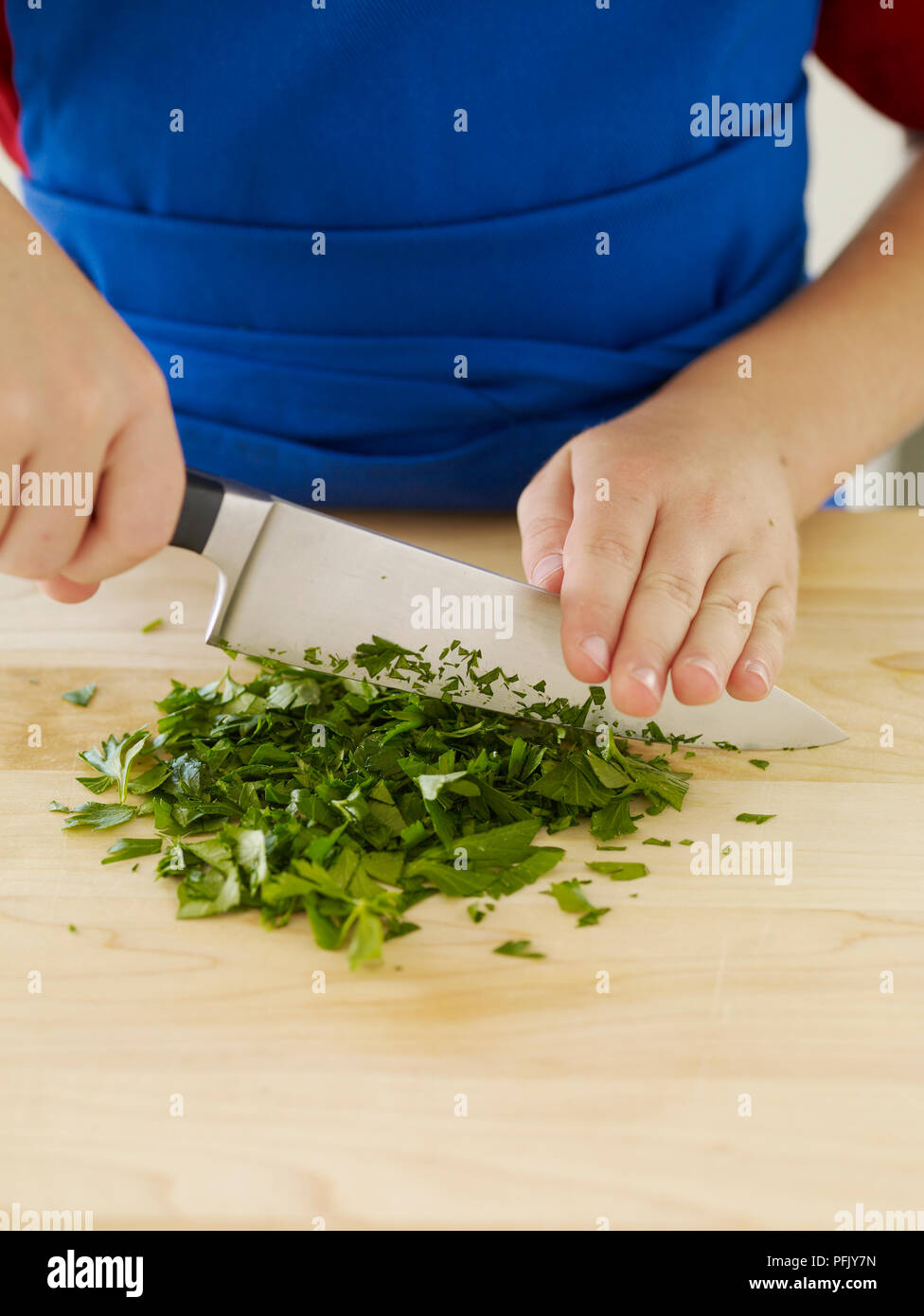 Boy's hands chopping herbs with large kitchen knife, closeup Stock