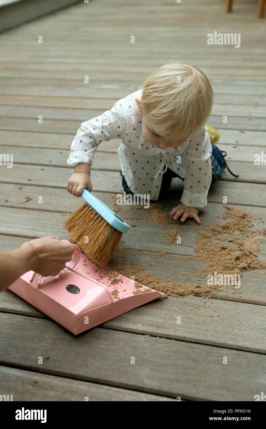 Blonde baby girl sweeping dust with brush, woman's hand holding dustpan ...