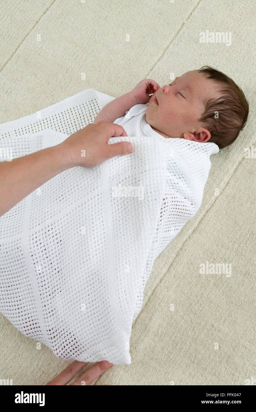 Swaddling a baby boy in a cellular blanket, close-up Stock Photo