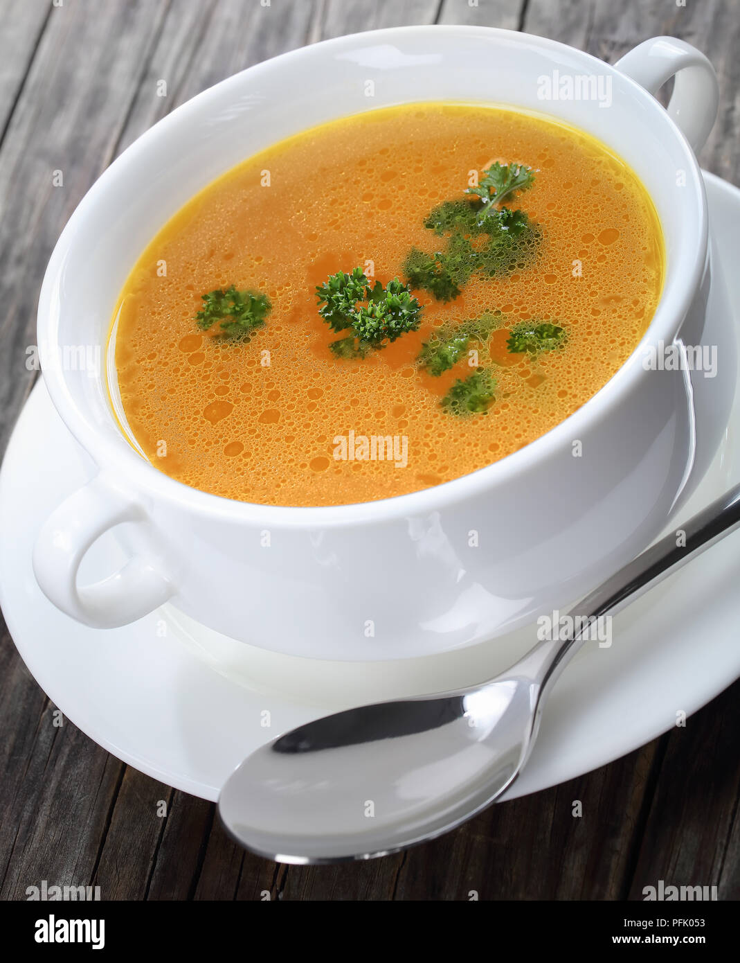 delicious Chicken broth with parsley in a white soup cup with spoon, view from above, close-up Stock Photo