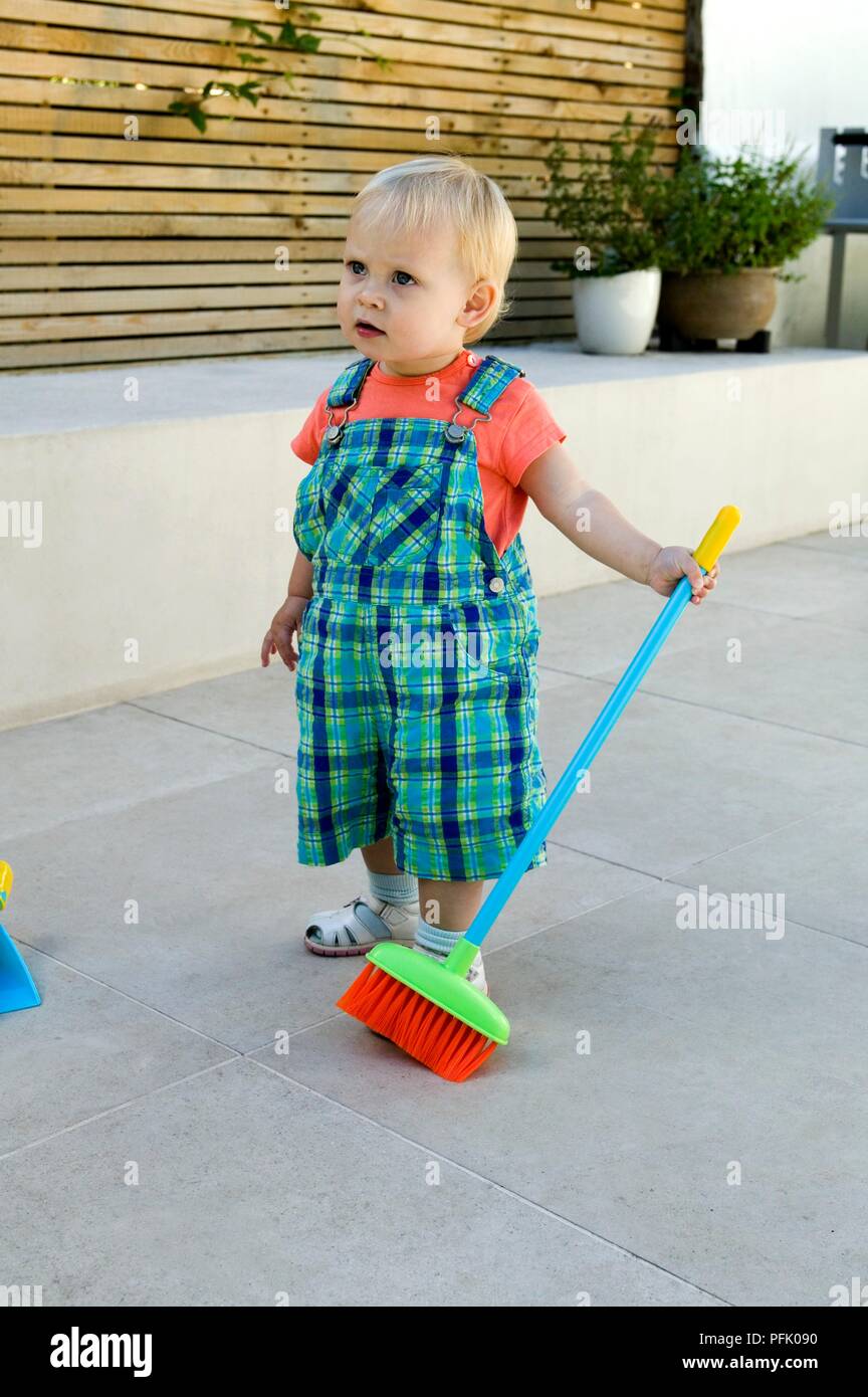Blonde baby girl standing on patio holding broom Stock Photo - Alamy