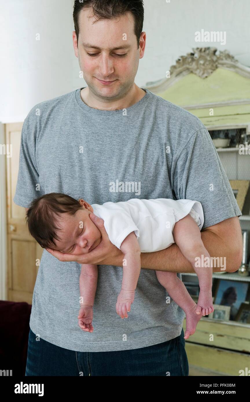 Baby boy lying asleep on man's arm with arms and legs dangling Stock