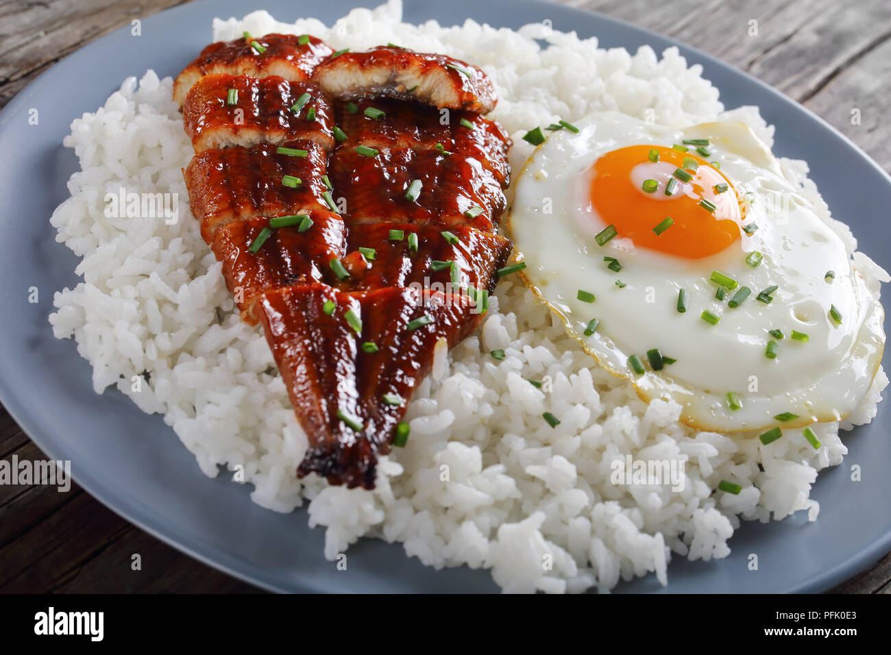 grilled unagi or eel with tare sauce sprinkled with chopped chives served with rice and fried egg on plate with chopsticks and tare sauce at backgroun Stock Photo