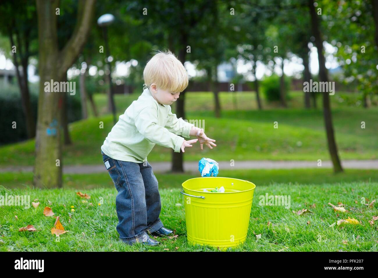 Blonde boy in park throwing rubbish in bin Stock Photo Alamy