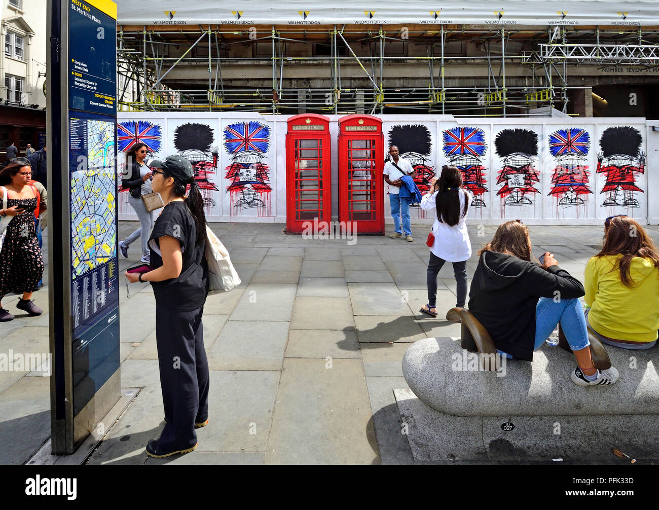 Tourists in St Martin's Place, London, England, UK. Traditional red telephone boxes and graffiti guardsmen by artist Nathan Bowendecorating constructi Stock Photo