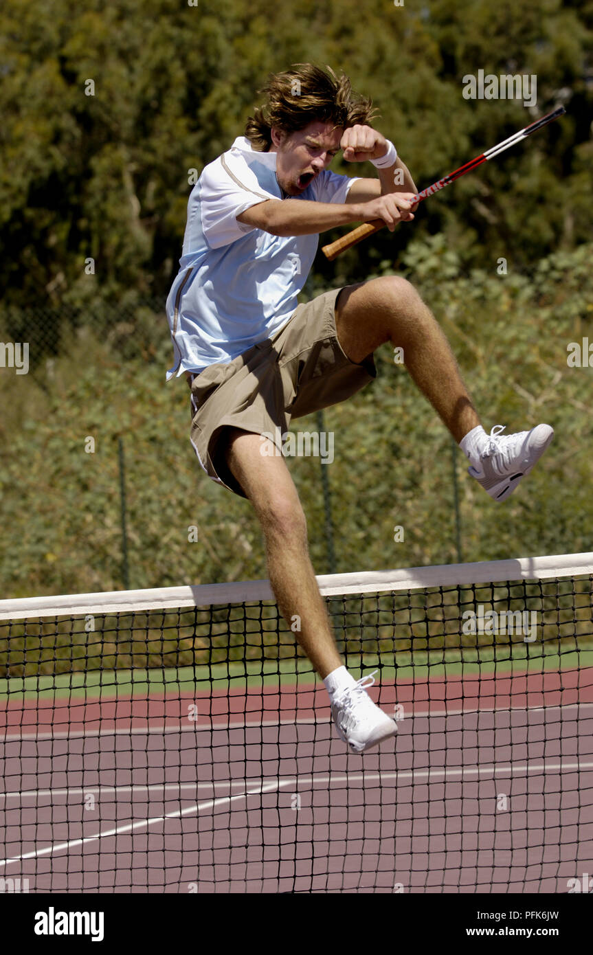 Male tennis player jumping over net after victory Stock Photo - Alamy