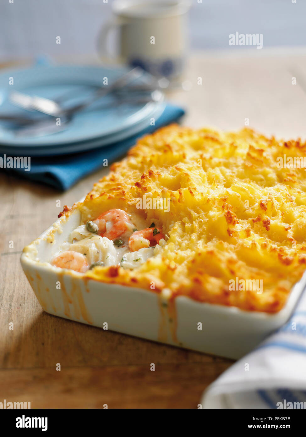 Fish pie in ceramic dish, plates, cutlery and mug in background Stock Photo
