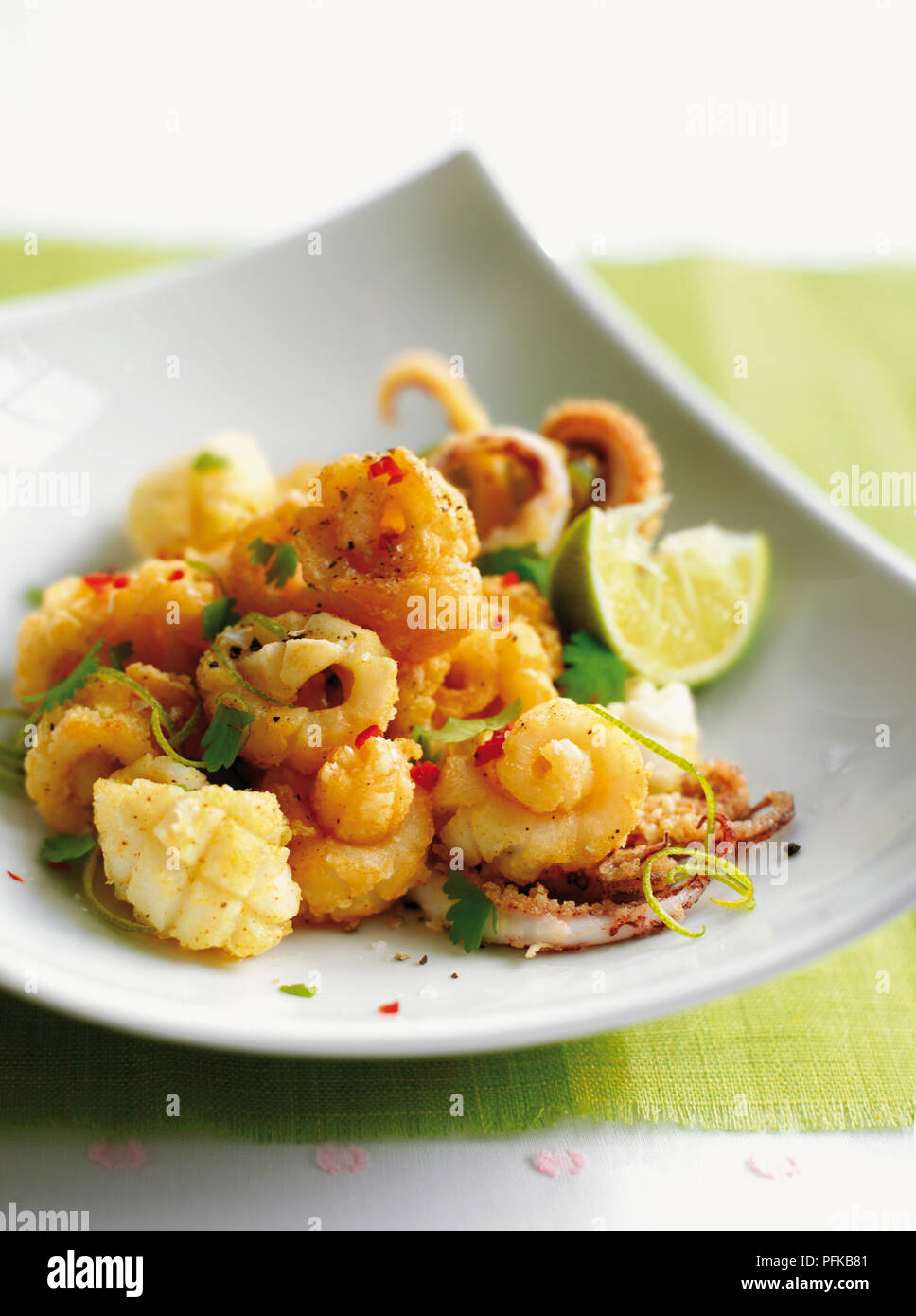 Deep-fried, cornflour coated squid, garnished with chilli, coriander leaves and lime, served on an angular plate Stock Photo