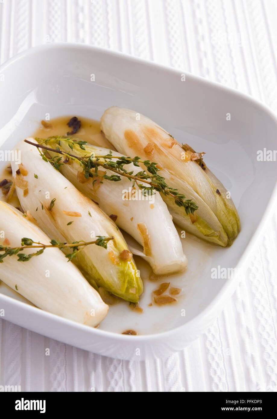 Braised chicory with shallots and thyme, in ceramic dish, on patterned tablecloth, close-up Stock Photo