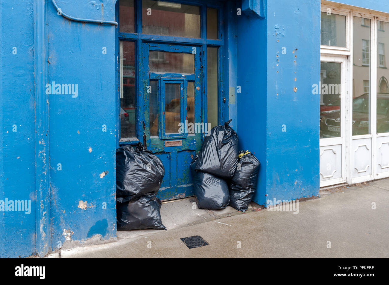 Full bin bags rubbish bags, dumped rubbish piled in a doorway in Skibbereen, West Cork, Ireland with copy space; Stock Photo